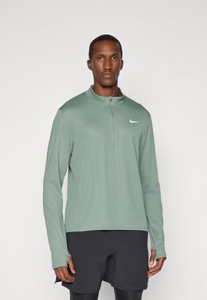 Grünes langärmliges Sportoberteil mit einem Reißverschlusskragen und Daumenlöchern, ausgestattet mit einem kleinen weißen Swoosh-Logo auf der linken Brust.