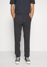 Grijze broek van een geweven stof met een slanke pasvorm, voorzien van steekzakken aan de voorkant, een knoopsluiting en gecombineerd met zwarte sneakers.