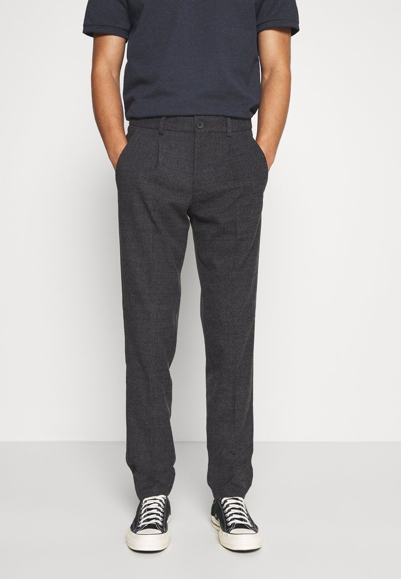 Grijze broek van een geweven stof met een slanke pasvorm, voorzien van steekzakken aan de voorkant, een knoopsluiting en gecombineerd met zwarte sneakers.