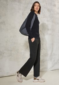 Marineblaues geripptes Sweatshirt, schieferfarbene, weite Hose, graue Schultertasche und beigefarbene Sneakers mit braunen Akzenten vor einem strukturierten hellen Hintergrund.