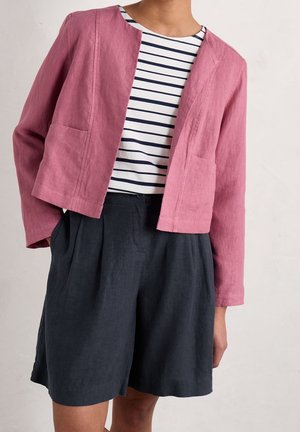 Giacca cropped in lino rosa con tasche laterali, abbinata a una maglietta a righe bianco e nera e pantaloni corti scuri, che mostra un fit rilassato.