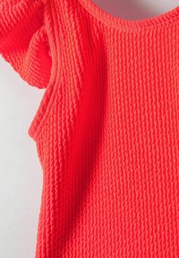 Haut en corail texturé et lumineux avec un motif ondulé, comprenant des manches courtes et un col arrondi. Tissu doux avec une apparence côtelée.