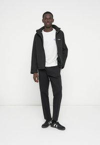 Black zip-up jacket, gray sweatshirt, and black pants. Model wears black sneakers with white stripes. Simple design, smooth textures.