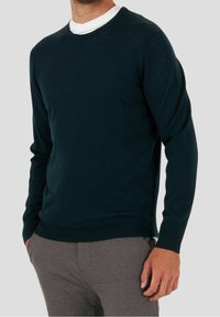 Diep groen gebreid sweater met lange mouwen en een ronde halslijn, gecombineerd met grijze broek, gladde textuur, minimalistisch ontwerp.