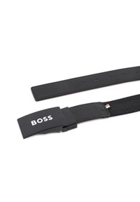 Μαύρη πλεκτή ζώνη με κομψό μαύρο μεταλλικό κούμπωμα, διαθέτει εμφανές λογότυπο "BOSS". Ομαλή υφή με οπές ρύθμισης κατά μήκος του ιμάντα.