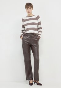 Gestreifter Strickpullover in Creme und Braun, kombiniert mit dunkelbraunen Lederhosen und burgunderfarbenen spitzen High Heels, die ein figurbetontes Design präsentieren.