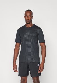 T-shirt de sport noir avec un motif géométrique texturé à l'avant, des manches courtes et un col rond, associé à un short noir.