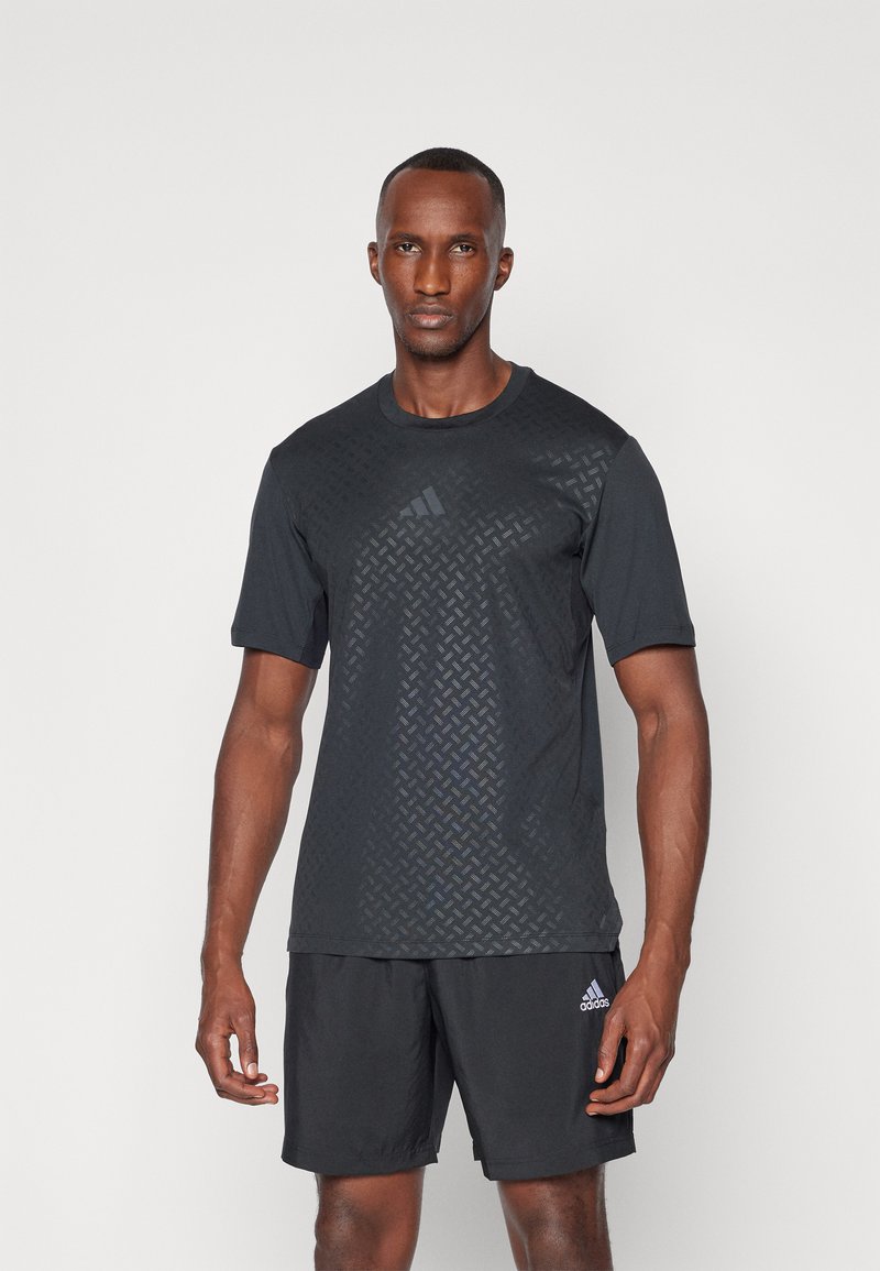 T-shirt de sport noir avec un motif géométrique texturé à l'avant, des manches courtes et un col rond, associé à un short noir.