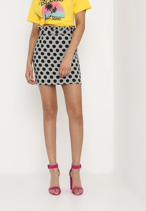 Zwart-wit gestreepte rok met grote zwarte polka dots, gecombineerd met een gele grafische t-shirt. Roze sandalen met hoge hak maken de outfit compleet.