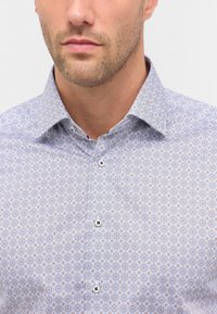 Lys blå button-up skjorte med et geometrisk mønster af små cirkler i hvidt og orange. Spidse kraver og synlige knapper.