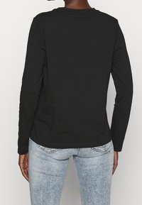 Svart långärmad skjorta i mjuk bomull, med rundad halsringning, figurnära passform och minimalistisk design; utan synliga logotyper eller detaljer.