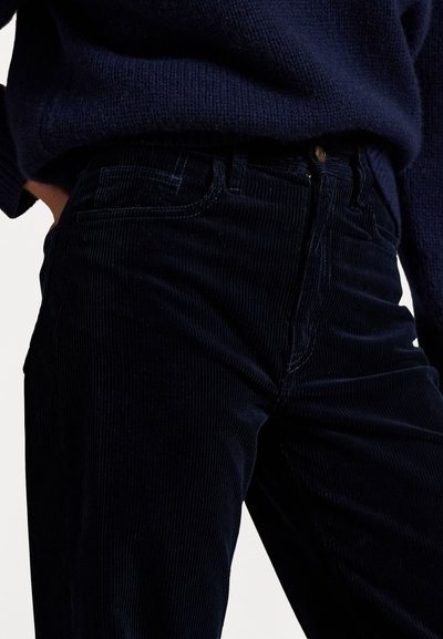 Navy corduroy pants with visible vertical ribs, a straight fit, and stitched pocket details. Brass button closure and zip fly.