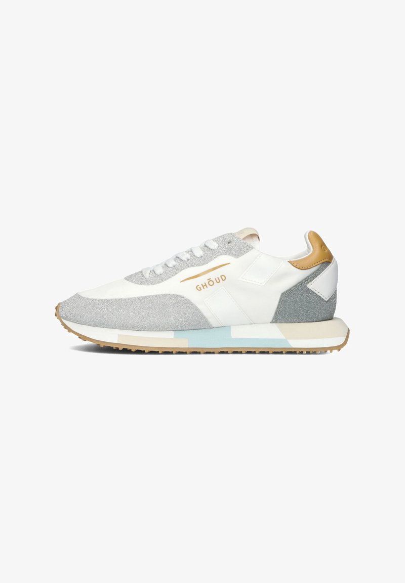 Witte sneaker met grijze en zilveren accenten. Heeft een gestructureerde bovenkant, platte witte veters, logo-detail en een lichtblauwe en beige zool.