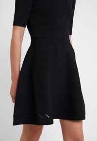 Abito nero realizzato in tessuto a maglia. Top aderente con maniche corte, gonna svasata e dettagli a zigzag sul bordo. Texture liscia in tutto il capo.