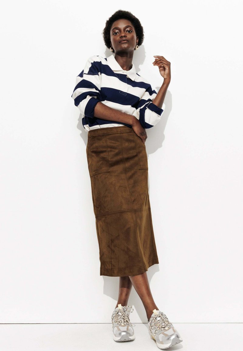 Polo à manches longues rayé bleu marine et blanc, jupe en daim brun, et baskets grises avec accents à motifs. Texture lisse, coupe décontractée.
