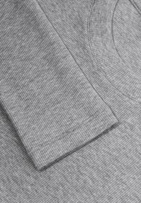 Szary longsleeve z ribbowym wzorem, okrągłym dekoltem oraz starannie wykończonym brzegiem o gładkim wykończeniu.