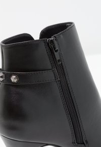 Schwarze Ankle-Boots aus glattem Leder, mit einem seitlichen Reißverschluss und einem dekorativen Riemen mit sechseckigen metallischen Akzenten.