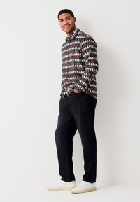 Musta nappipaita, jossa värikäs joulukuosi, yhdistetty tummiin housuihin ja valkoisiin lenkkareihin. Kokonaisuudessaan rento asu.