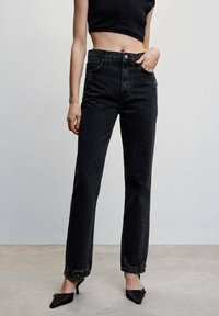 Jeans de mezclilla negros de pierna recta con cintura alta, ligeros desgarros en el dobladillo y bolsillos frontales. Combinados con un top negro corto y tacones negros elegantes.