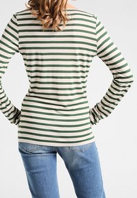 Striped long-sleeve top in green and cream, featuring a boat neckline and fitted silhouette. Paired with blue jeans, showing a casual style.