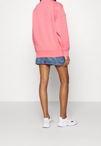 Růžová oversized mikina, denimová mini sukně, bílé atletické boty. Texturovaná látka s kleslými rameny, žebrovanými manžetami a lemem.