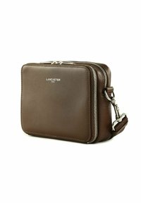 Borsa a tracolla in pelle marrone con zip, hardware argentato e cuciture a contrasto. Nome del marchio "Lancaster" impresso sul davanti.