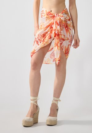 Blommig omslagskjol i genomskinligt tyg, med orange och persikotoner och knytning i midjan. I kombination med beige espadrillos.