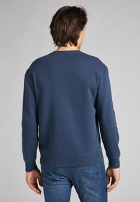 Mörkblå sweatshirt i bomullsmix, med klassisk rund hals, ribbade ärmslut och nederkant. Slät textur utan synliga mönster.