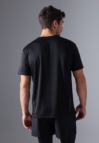 Črna kratkolasna športna majica z gladko teksturo, rahlim sijajem in odsevnimi detajli ob straneh, zasnovana za aktivno nošenje.