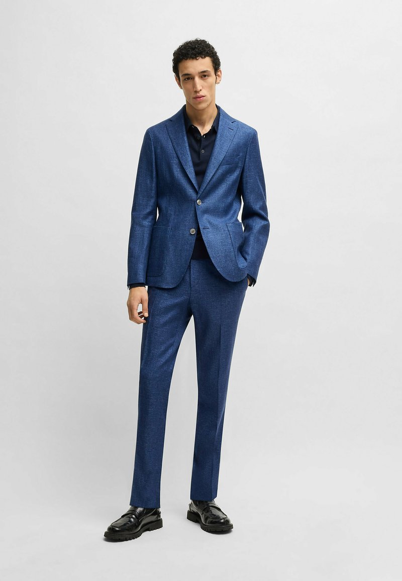 Blue suit made of textured fabric, featuring a single-breasted jacket with a notch lapel, slim-fit trousers, and black shoes.