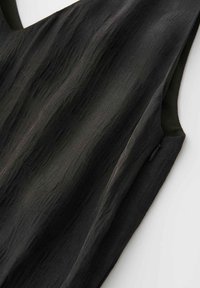 Black textured sleeveless top with side zipper detail on a white background.