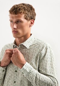 Lichtgroene en witte overhemdbloes met een geometrisch patroon. De stof lijkt textuur te hebben, met knoopmanchetten en kraagdetails.