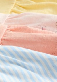 Közeli kép összehajtogatott, puha pamut anyagokról sárga, rózsaszín, őszibarack és kék-fehér csíkokkal, redőzött varrási részletekkel.