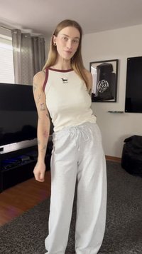 Canotta bianca con bordi bordeaux che presenta una stampa di un cane, abbinata a pantaloni della tuta grigi chiari con vita elastica.