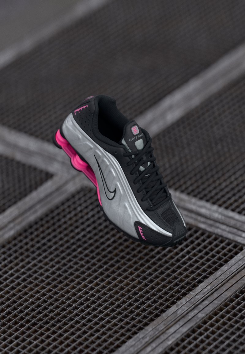Czarno-srebrne buty do biegania Nike z różowymi akcentami zawieszone nad metalową siatką, podkreślające smukły design i amortyzację.
