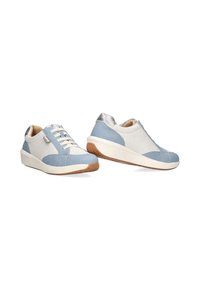 Zapatillas azul claro y blancas con tela texturizada, detalles plateados y suelas de goma. Presentan un diseño de cordones y punta redondeada.