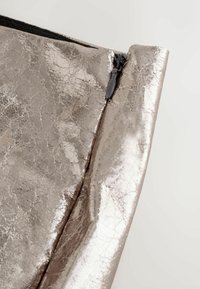 Metallisch silberne Tasche mit strukturierter Oberfläche und sichtbaren Falten. Verfügt über einen schwarzen Reißverschluss entlang der Oberkante zum Verschließen.