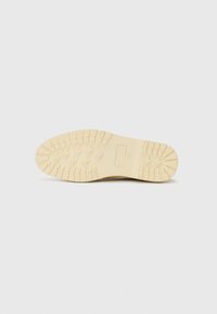 Rubber sole in beige with a textured, patterned tread. Features a central rectangular accent with embossed detailing. Smooth edges.