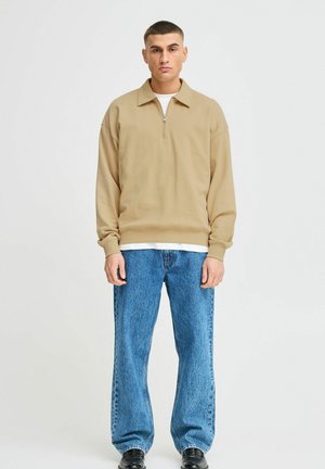 Beige quarter-zip sweatshirt with a relaxed fit, long sleeves, and ribbed hem, paired with light blue baggy jeans and black shoes.