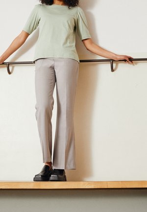 Hellgrünes Kurzarmhemd mit lockerem Schnitt, kombiniert mit grauer, maßgeschneiderter Hose und schwarzen, zum Hineinschlüpfen geeigneten Schuhen, die eine glatte Textur zeigen.