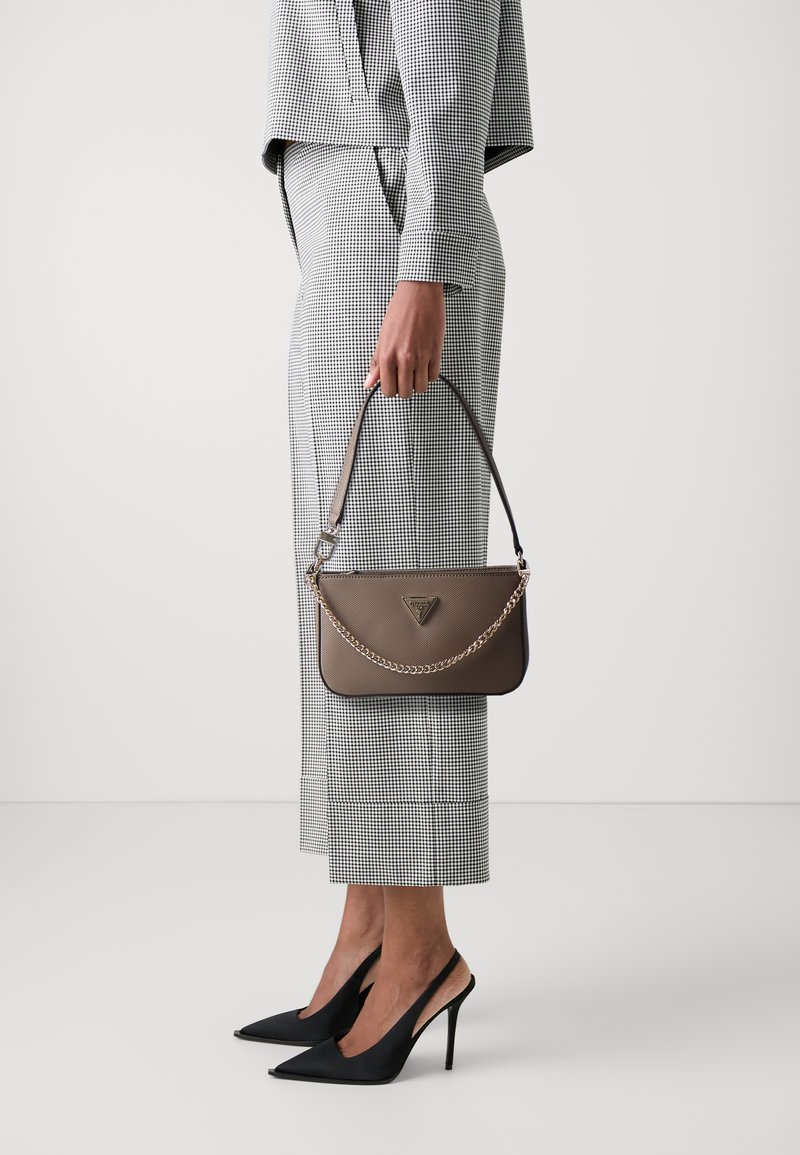 Brun lærveske med kjedestropp, rektangulær form, med merkevaren sin logo. Modellen har på seg en svart og hvit rutete dress og høye hæler.