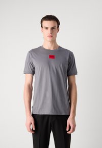 Grå bomulds t-shirt med korte ærmer og rund hals. Har en rød firkantet lap med "HUGO" tekst i midten foran.