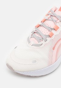 Gros plan d'une chaussure de course Nike blanche et rose avec des lacets gris et un tissu en maille respirant sur fond blanc.