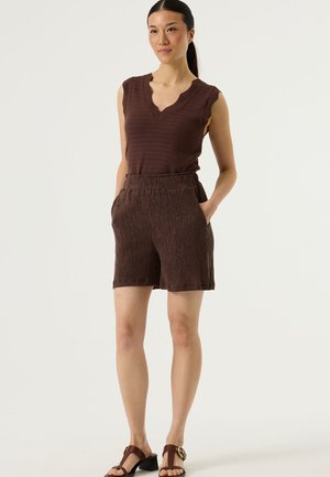 Débardeur marron texturé avec un col en forme de festons, accompagné d'un short marron à motifs avec des poches latérales, porté avec des sandales à talons.