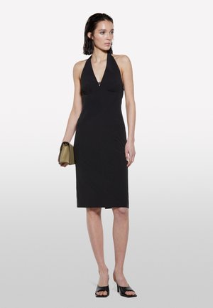Schwarzes Halterneck-Kleid mit taillierter Silhouette, das an der Vorderseite Raffungen aufweist und einen knielangen Saum hat. Modell hält eine kleine olivgrüne Tasche.
