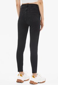 Schwarze Skinny-Jeans mit hoher Taille, die eine glatte Denim-Oberfläche und zwei Gesäßtaschen haben, kombiniert mit weißen und orangen klobigen Sneakern.