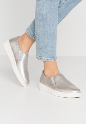 Metallic sølv slip-on sko med en tekstureret finish, der har elastiske sidesegmenter og en hvid gummisål. Båret med lyseblå jeans.