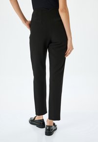 Zwarte high-waisted broeken met een getailleerde pasvorm, met een zachte textuur en subtiele pintuck-details aan de achterkant. Gecombineerd met zwarte schoenen.