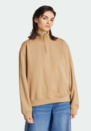 Sweat à zip beige avec un col montant et une coupe décontractée, présentant un logo Adidas tonal sur la poitrine et des poignets côtelés.