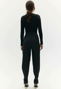Zwarte lange mouwen top en hoge taille zwarte broek. Glad textuur, aansluitende top met een slanke silhoutte. Schoenen met gouden accenten.